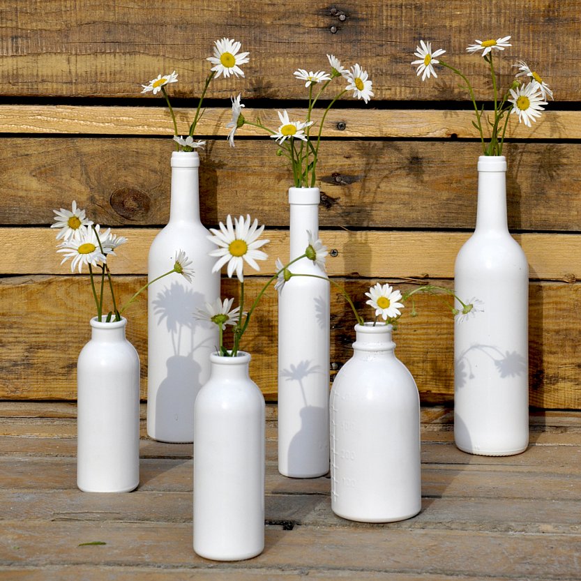 Покрашенные в белый цвет бутылки разных форм летняя альтернатива цветочным вазам.